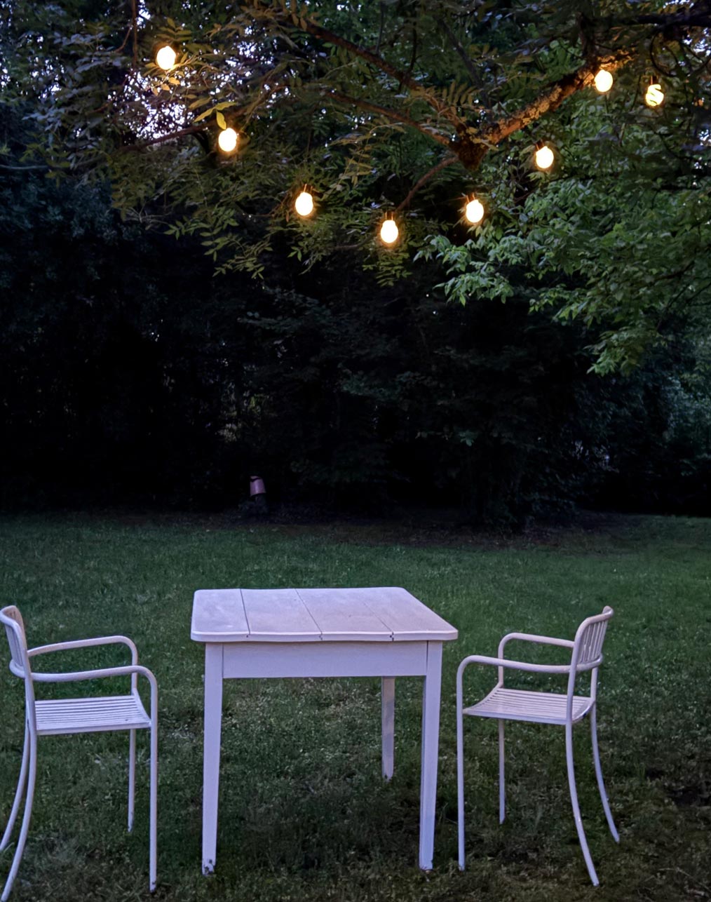Table de jardin illuminée par une guirlande lumineuse au crépuscule, à l'Atelier Latresne