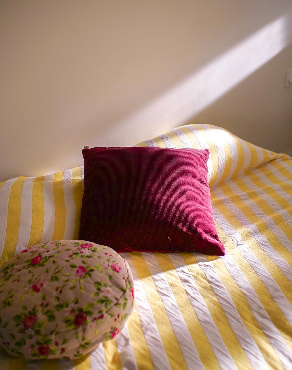Lit avec linge rayé jaune et blanc et coussins dans la suite de l'Atelier Latresne